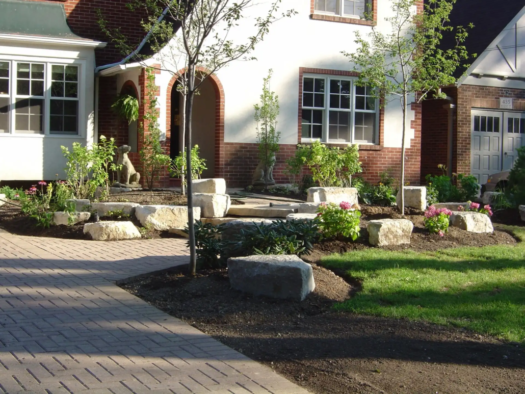 Paver surface connecting to natural stone front steps and planting beds beside a house.